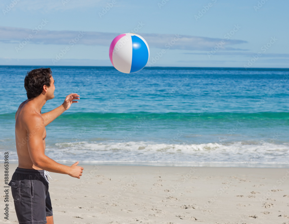 Obraz premium Inflatable beach ball is hovering above sunlit sandy shoreline, with turquoise ocean beyond