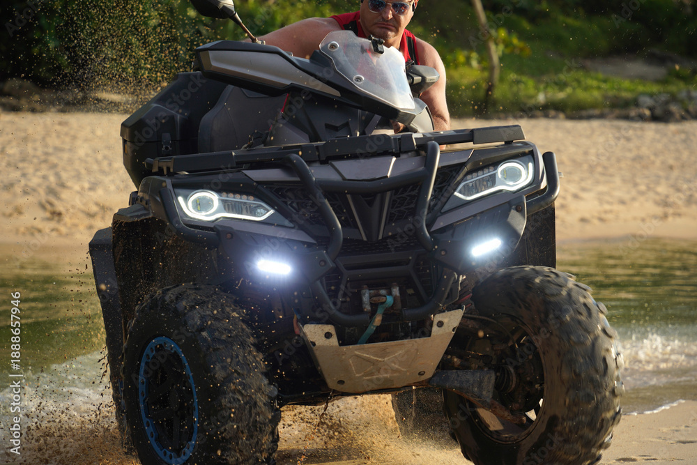 Fototapeta premium A man engages in extreme ATV riding on sand beach early in the morning