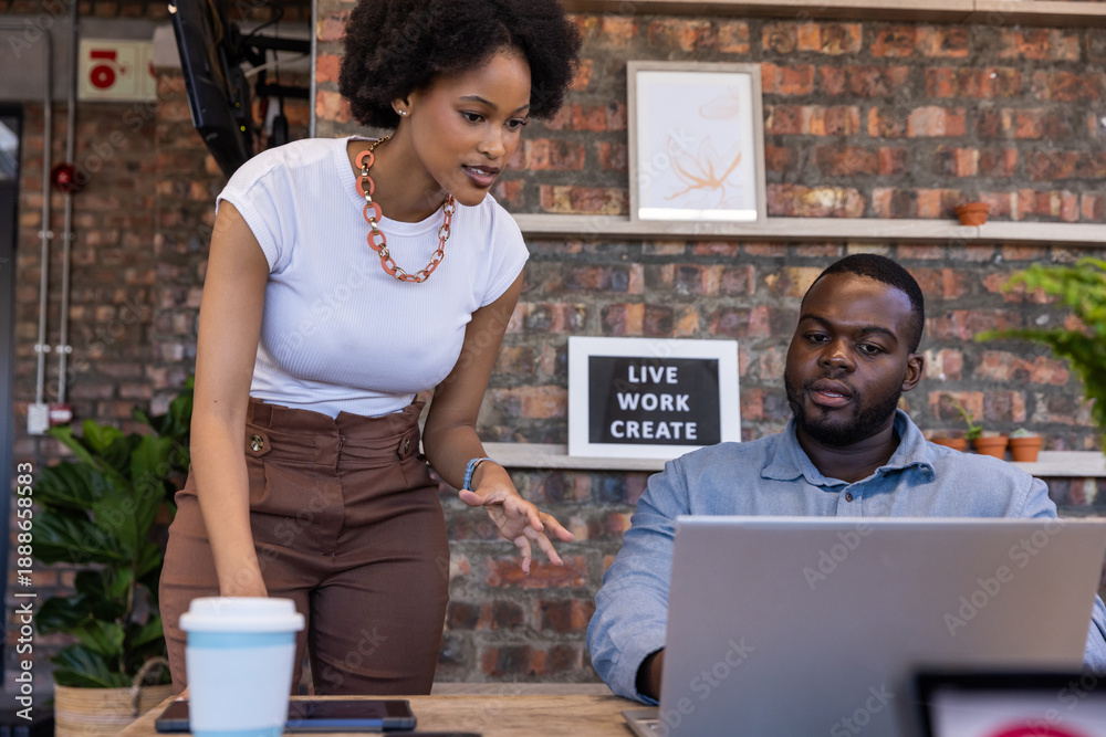 Fototapeta premium African american colleagues collaborating at desk in office with tablet coffee cup and sign