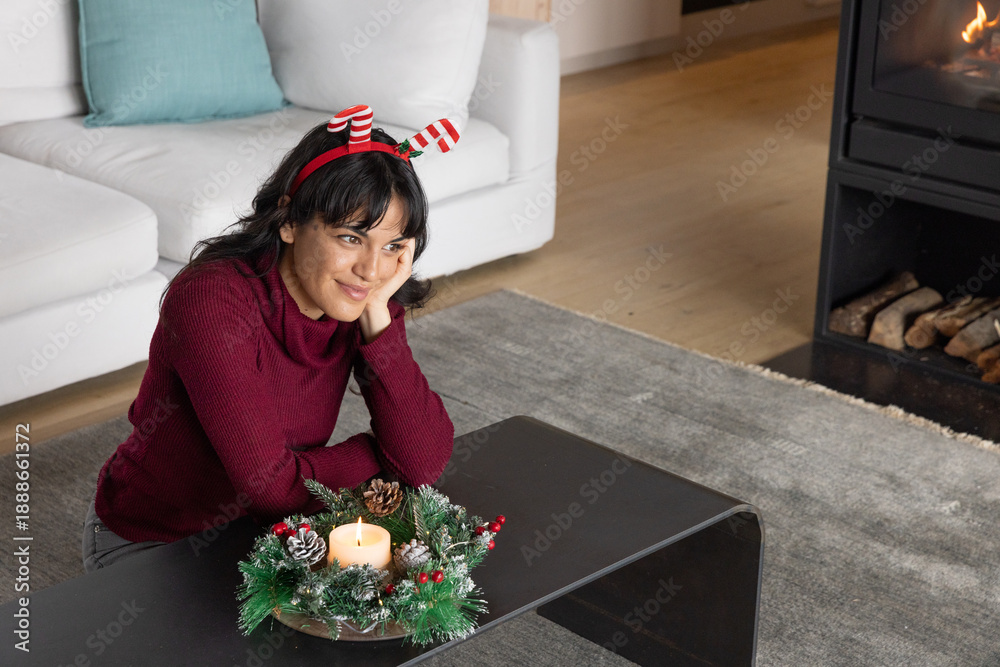 Naklejka premium Asian woman sitting at coffee table in living room wearing headband viewing evergreen wreath