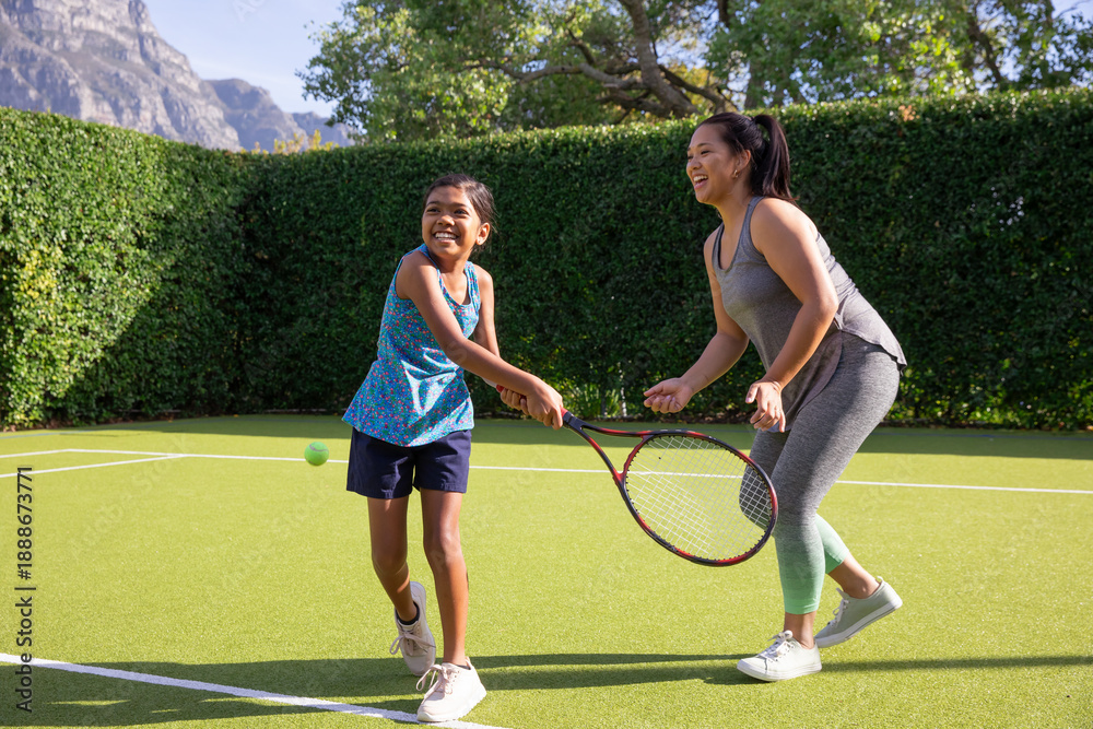 Obraz premium Asian mother and daughter swinging tennis rackets while playing on private, garden court