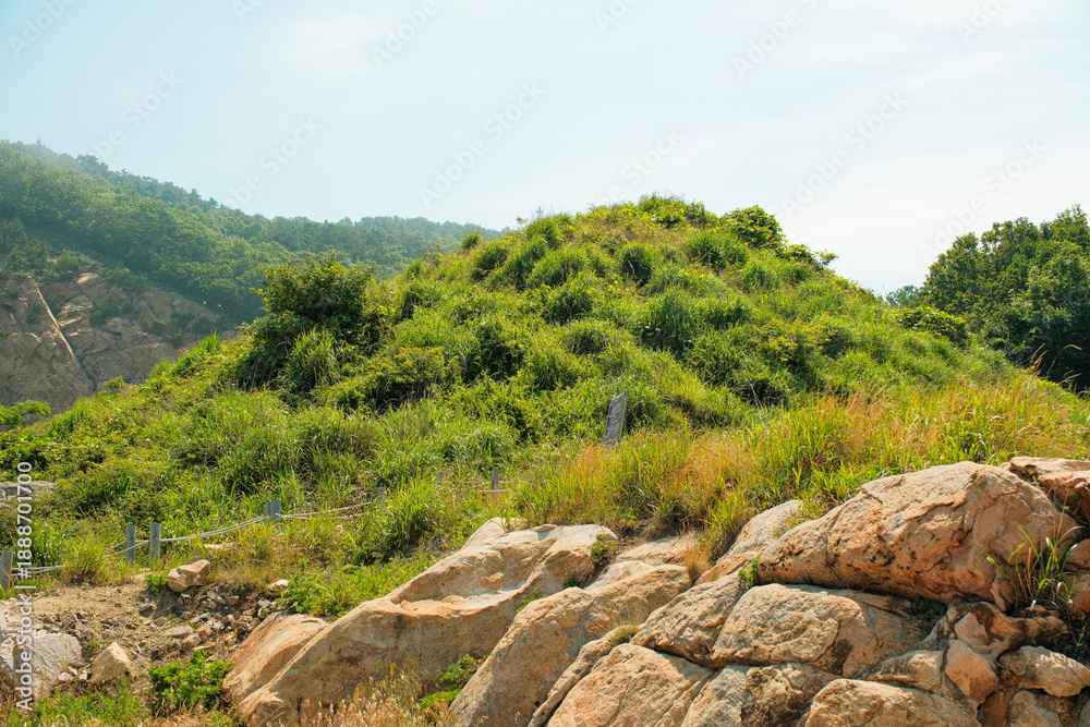 Fototapeta premium Everyday scenery on Pungdo Island, South Korea, showing small rural structures, green hills, coastal vegetation, and a quiet walking path that reflect
