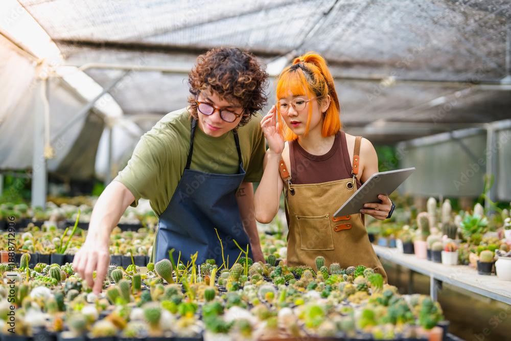 Fototapeta premium Young Asian Man and Woman Cactus Farm Owners Caring for Plants Together, Using Tablet for Small Eco-Friendly Business