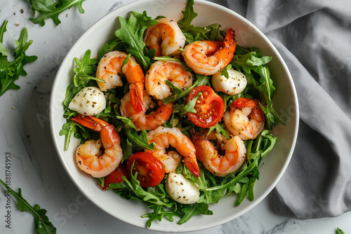 Baked shrimp, mozzarella, and arugula salad in a white bowl with a grey cloth background.