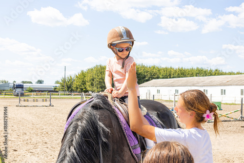 Little girl in safety helmet taking her first horse riding lesson with instructor