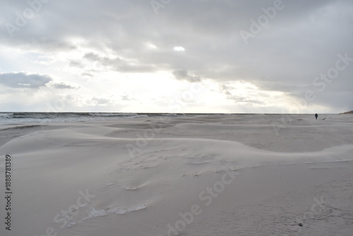 Dramatic stormy sky over an empty sandy beach with waves and dark clouds. Moody seascape landscape with strong wind, cold atmosphere and vast open space. Minimalist coastal scenery, solitude and natur