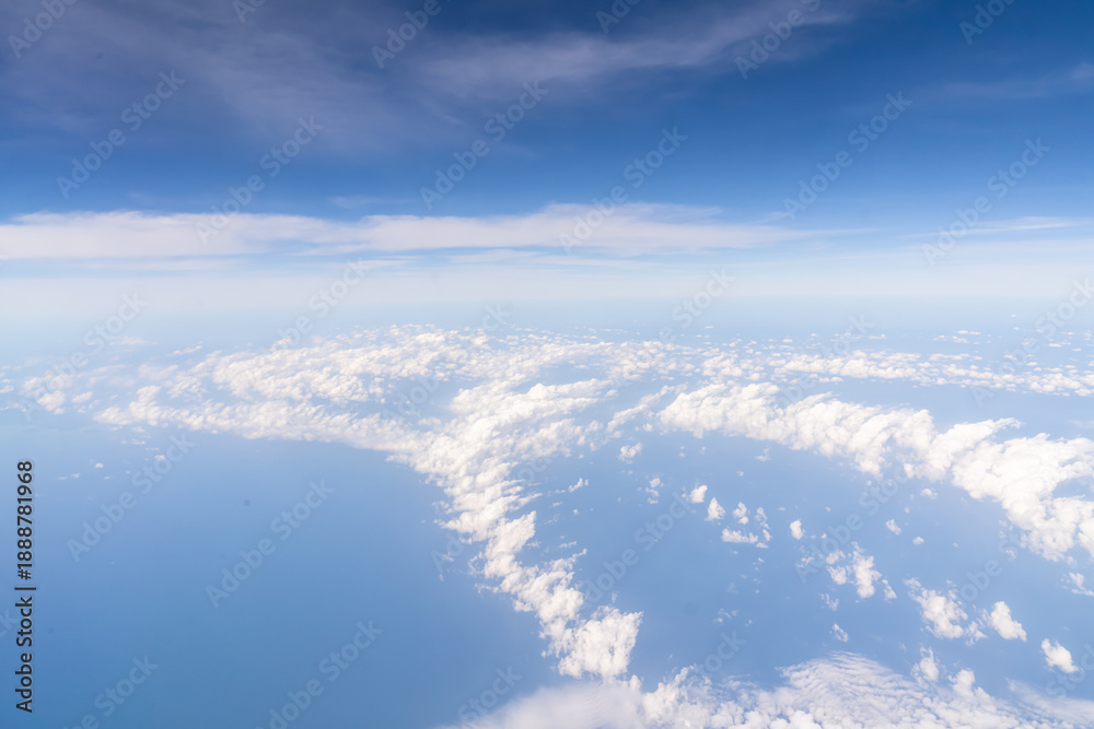 Naklejka premium Clouds are visible above the vast ocean from an airplane window. The sky is mostly blue with some clouds. This scene shows the expanse of nature from a high point in the sky. High quality photo