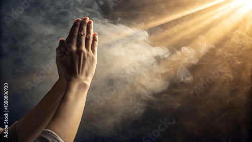 Hands clasped in prayer with divine light shining through smoke