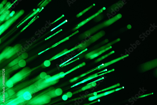 Abstract green fiber optic light streaks on dark background, glowing bokeh lines symbolizing data flow and technology.