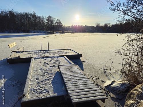 A pier and a bench on the frozen lake on a sunny winter morning.