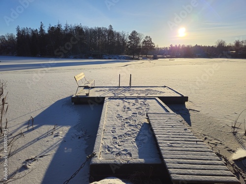 A pier and a bench on the frozen lake on a sunny winter morning.