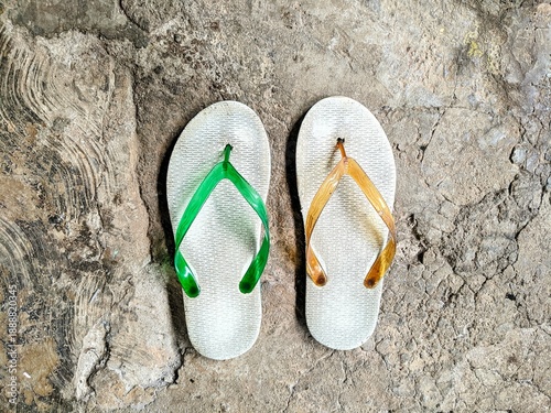 Fotografía Top view of worn-out flip-flops with green and orange straps on a cracked concrete floor