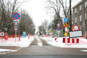 Road construction and traffic signs on snowy city street. Temporary detour and roadworks in winter. Urban infrastructure maintenance. Restricted access street with warning signs and barriers.