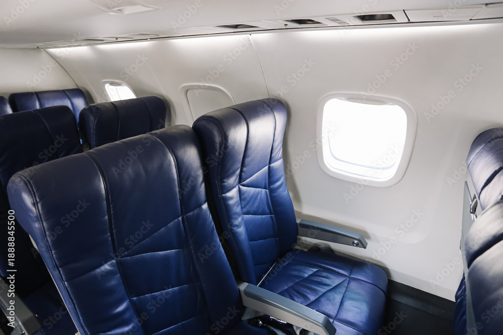 Obraz premium Empty airplane cabin interior with blue leather seats. Passenger seating row by window. Commercial aircraft economy class detail. Air travel comfort and transportation concept.