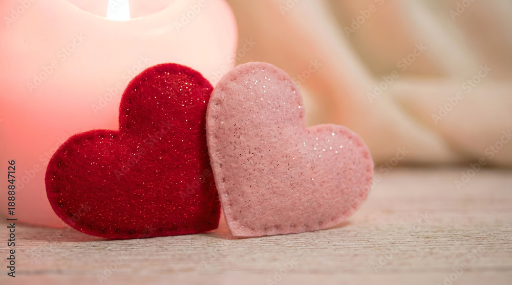 Obraz premium Two soft felt heart shapes one red one pink sparkling gently beside a glowing candle on wooden surface