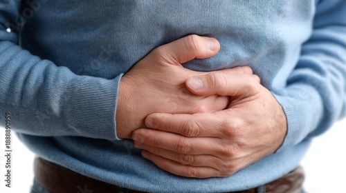 A man is wearing a blue sweater and holding his stomach. Concept of discomfort and pain, as the man's hand is placed on his stomach