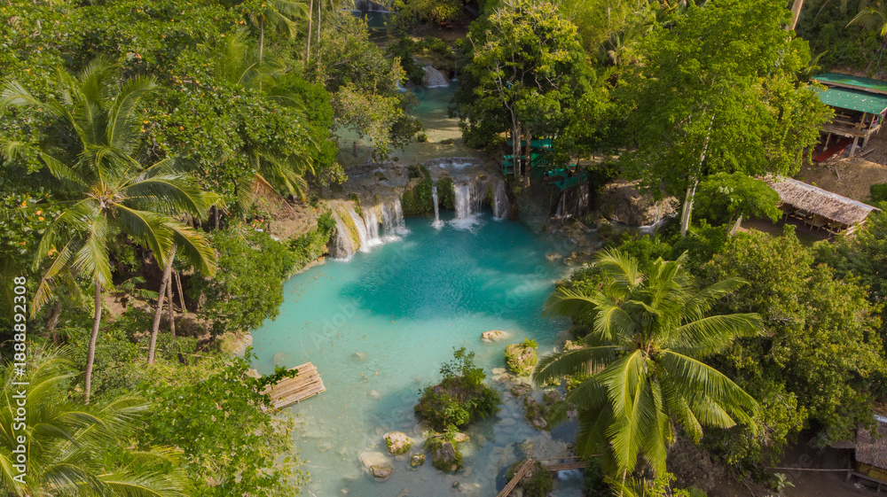 Fototapeta premium Drone aerial view of Cambugahay Falls in Siquijor, Philippines, featuring turquoise freshwater pools surrounded by lush tropical jungle and palm trees, showcasing a popular tropical travel destination