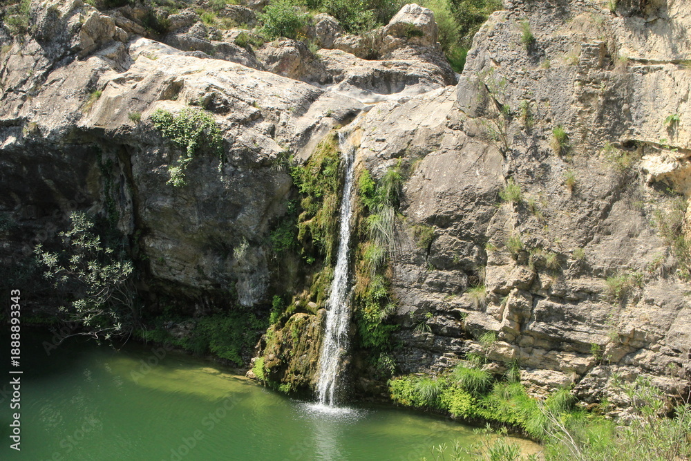 Fototapeta premium Waterfall flowing down rocky cliff into green pool, peaceful canyon nature scene