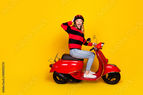Charming Young Woman Posing on a Red Scooter with Cheerful Expression Against Vibrant Yellow Background