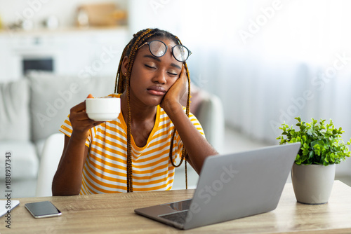 Obraz na plátně Exhausted millennial black woman freelancer sitting in front of laptop with cup