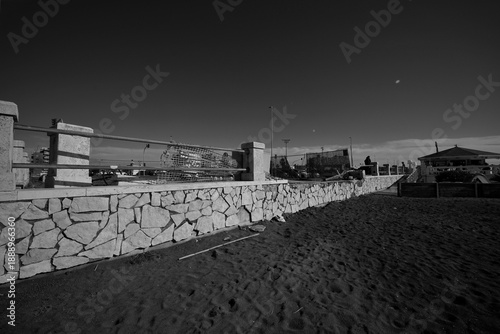 Konstfotografi Ostia, Rome, Italy - January 25, 2026, section of a travertine retaining wall in opus incertum with perspective view of a stretch of public beach near the Hakuna Matata kiosk