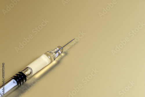 Glass syringe filled with transparent liquid lying horizontally on a soft yellow background, minimal medical still life symbolizing vaccination, cosmetic filler, insulin injection and healthcare.