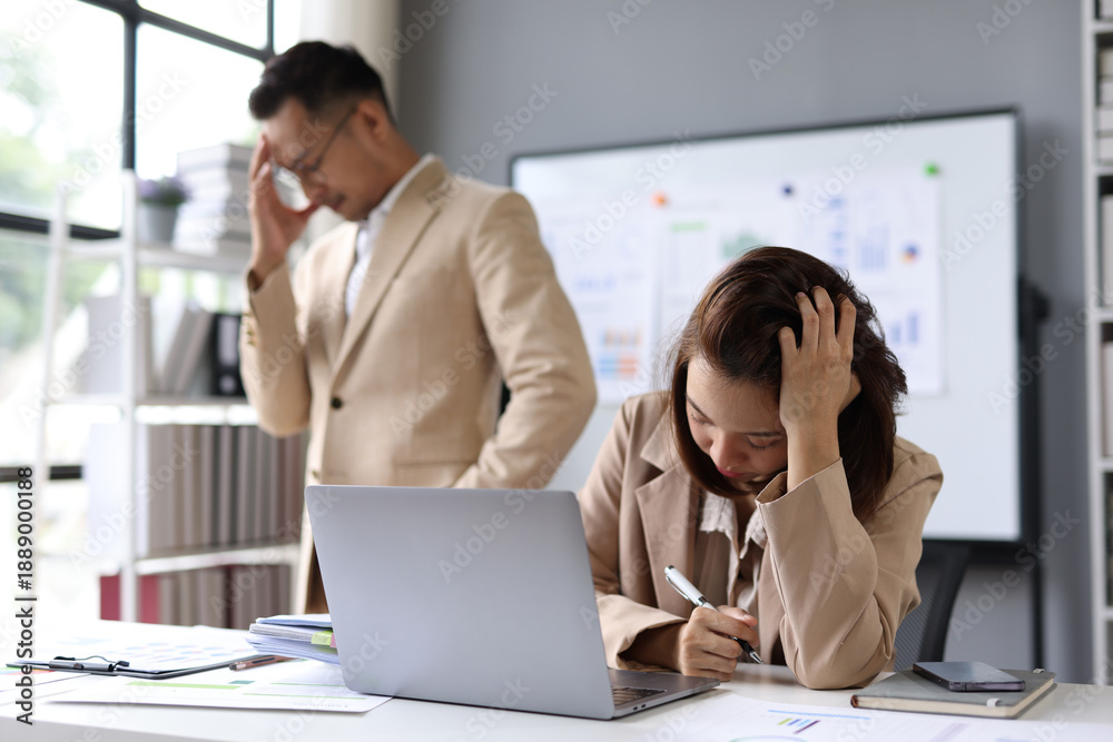 Obraz premium Young stressed businesswoman with listening to her angry manager complaining about work while sitting at office desk in front of laptop.