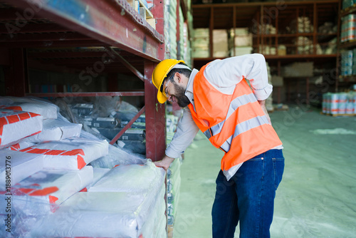 Foto Industrial worker experiencing back pain while lifting heavy bags in a warehouse