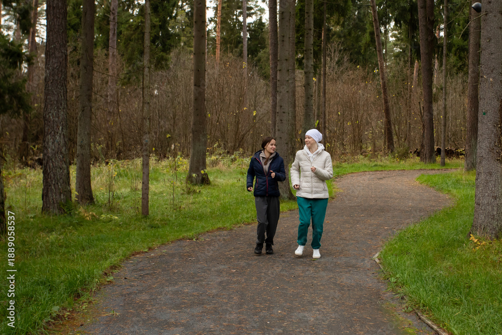 Fototapeta premium Two women jogging on forest path in autumn, concept of support, friendship, and healing through physical activity.