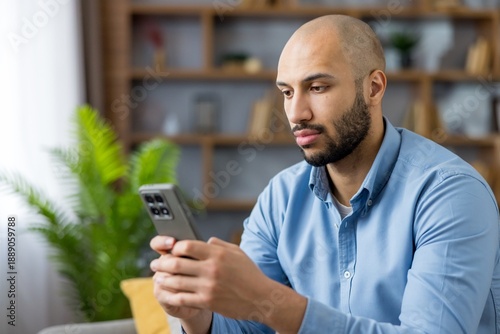 Foto Young bald man focused on smartphone screen, browsing social media and messaging
