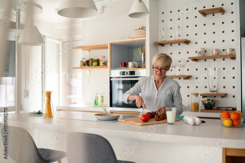 Bilde på lerret Senior woman preparing a healthy meal in a bright modern kitchen with natural mo
