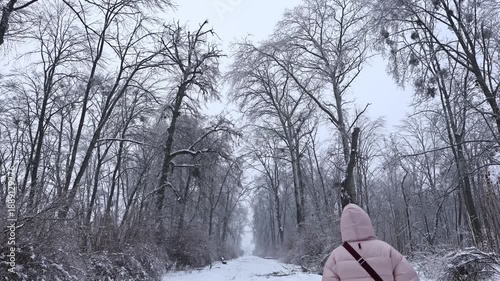 Young woman in pink down jacket walking along snowy path in frozen winter park