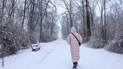 Young woman in pink down jacket walking along snowy path in frozen winter park