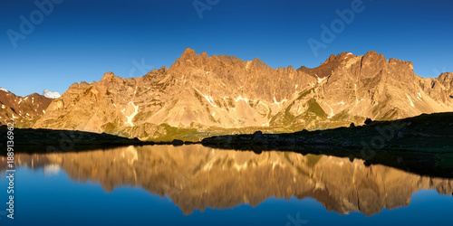 Sunrise at Laramon Lake, Still water of alpine mountain lake reflecting rocky peaks of the Cerces Massif, French Alps. Panoramic natural landscape in the Claree Valley, Hautes-Alpes