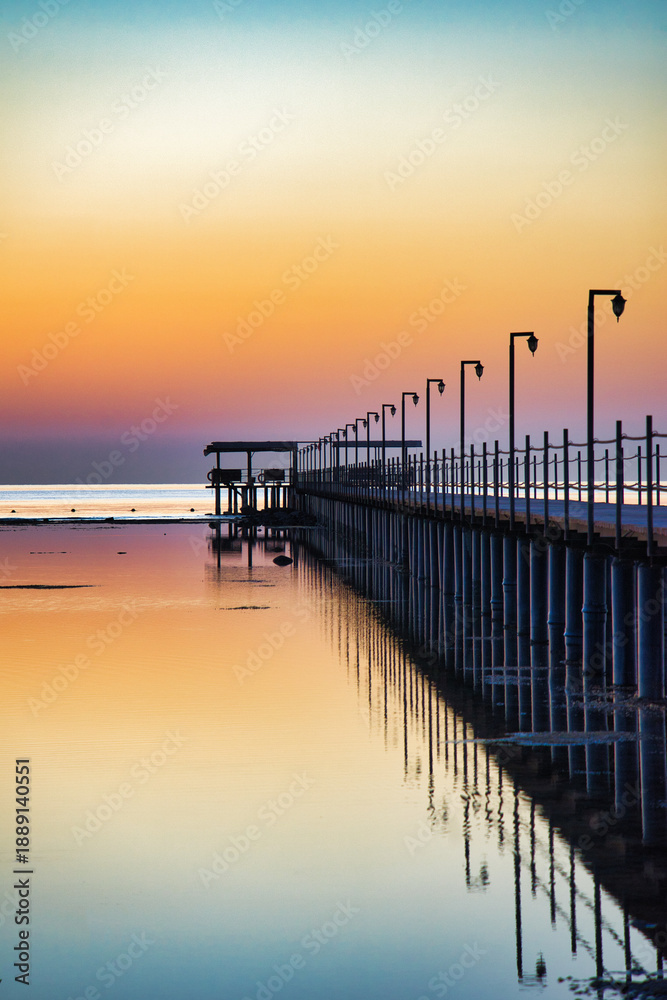 Obraz premium A breathtaking sunset over the Red Sea in Egypt, with a long wooden pier stretching across calm, reflective water.