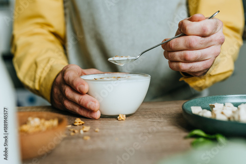Man eating yogurt with granola in bowl on wooden table