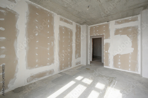 Fotografie Unfinished room with gypsum board walls, exposed concrete ceiling and floor, electrical outlet visible, doorway open, awaiting final plastering and painting