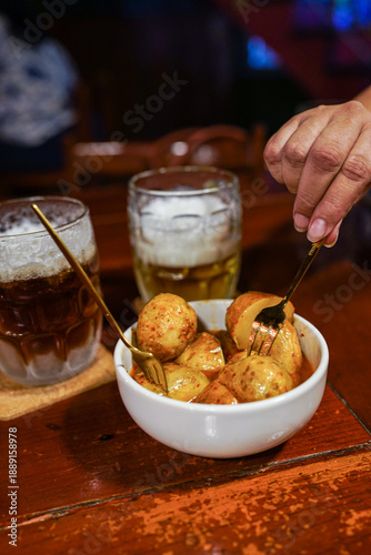 Person eating spicy Patatas Bravas tapas with beer