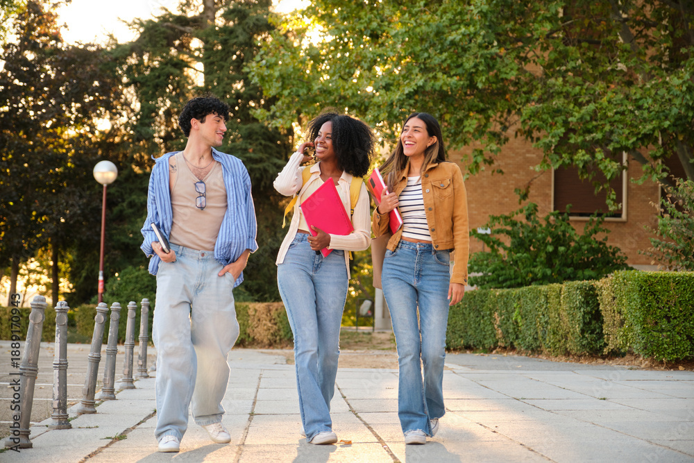 Fototapeta premium Group of diverse university students walking campus together smiling and talking, holding notebooks