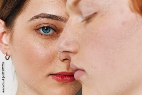Portrait of two young women with different skin tones close together, showing facial features, eye detail, natural expression and minimal makeup in studio lighting.