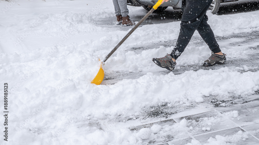 Naklejka premium Snow cleaning service worker shoveling snow from driveway with bright yellow shovel, showcasing winter maintenance and outdoor labor efforts