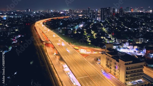 Drone view of nighttime car lanes, highway, and intersections in the city, city road, car lanes, expressway between buildings, traffic flow on city road, expressway and highway, traffic junction car