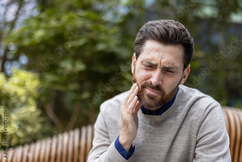Εκτύπωση καμβά Close-up photo of a young man sitting on a bench, holding his cheek with his han