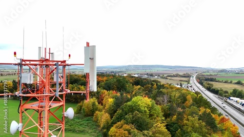 Drone view of telecommunications tower with antennas above green fields and trees. Modern wireless infrastructure transmitting mobile network signals, concept of communication technology and connectiv