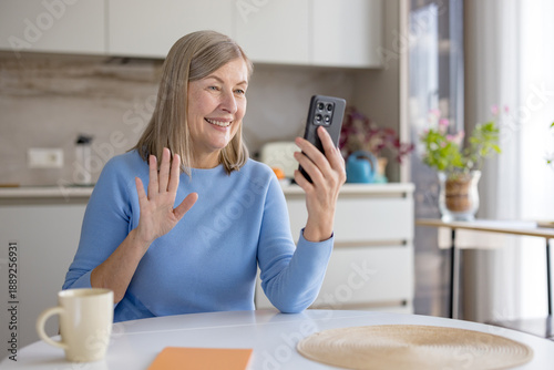 Photos Senior woman at home smiling and waving during a smartphone video call, enjoying