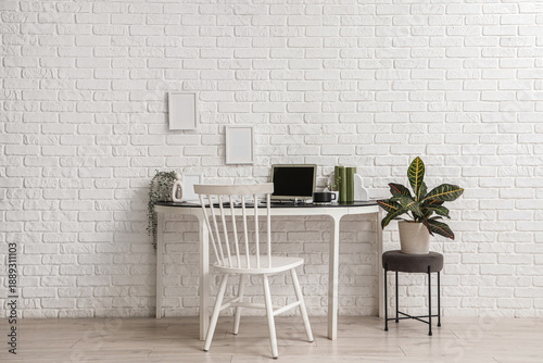Workplace with laptop and coffee cup near white brick wall in office
