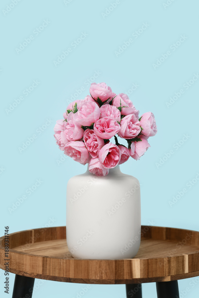 Obraz premium Vase with artificial pink flowers on table near blue wall