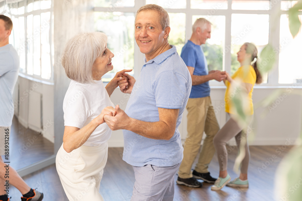 Fototapeta premium Happy smiling elderly man enjoying impassioned merengue with female partner in latin dance class. Social dancing concept..