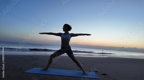 Silhouette of a woman practicing yoga on the beach at sunrise