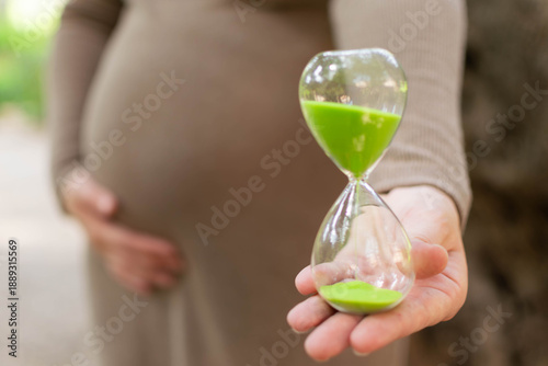 Fotografie mujer embarazada soteniendo en una mano un reloj de arena contando el tiempo que